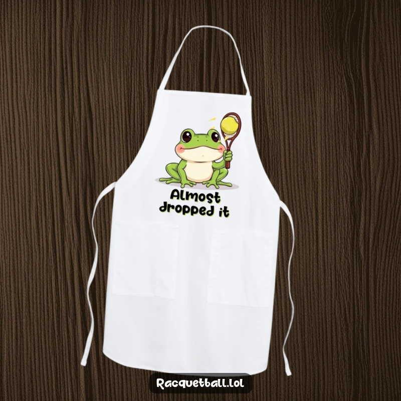 Funny apron showing a frog with wide eyes watching a racquetball zoom past, a humorous kitchen accessory for the amused observer.