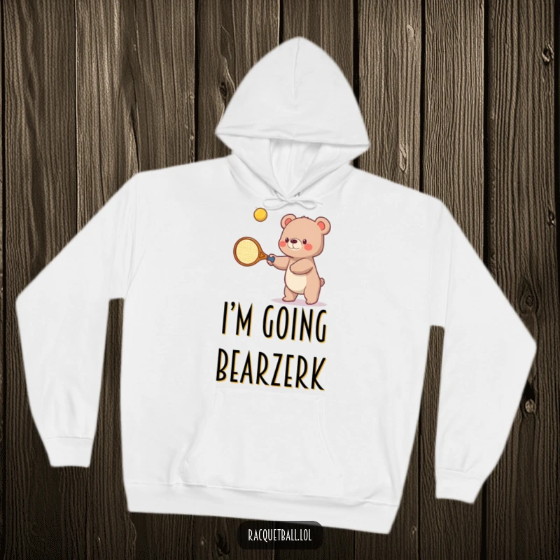 Funny hoodie depicting a small bear with a comically oversized tennis racquet, playfully hitting a bouncing ball upwards during a tennis match.